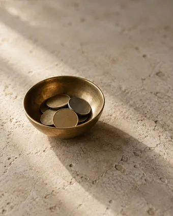 A small brass bowl of coins on cream stone